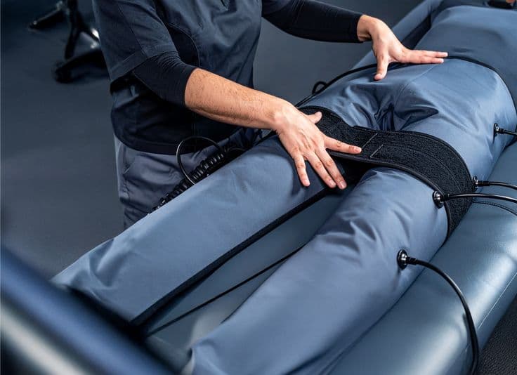 Aplicação de pressoterapia com profissional ajustando botas de compressão nas pernas